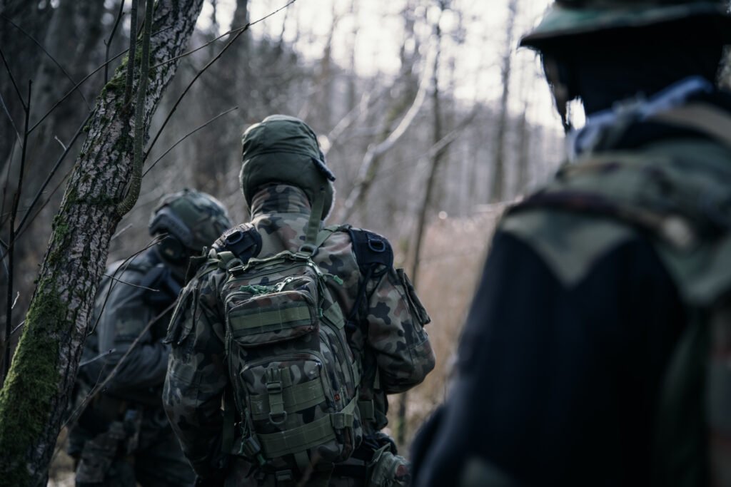 Widok z tyłu na trójkę Strzelców w kamuflażu wz. 93 idących jeden za drugim w terenie leśnym.